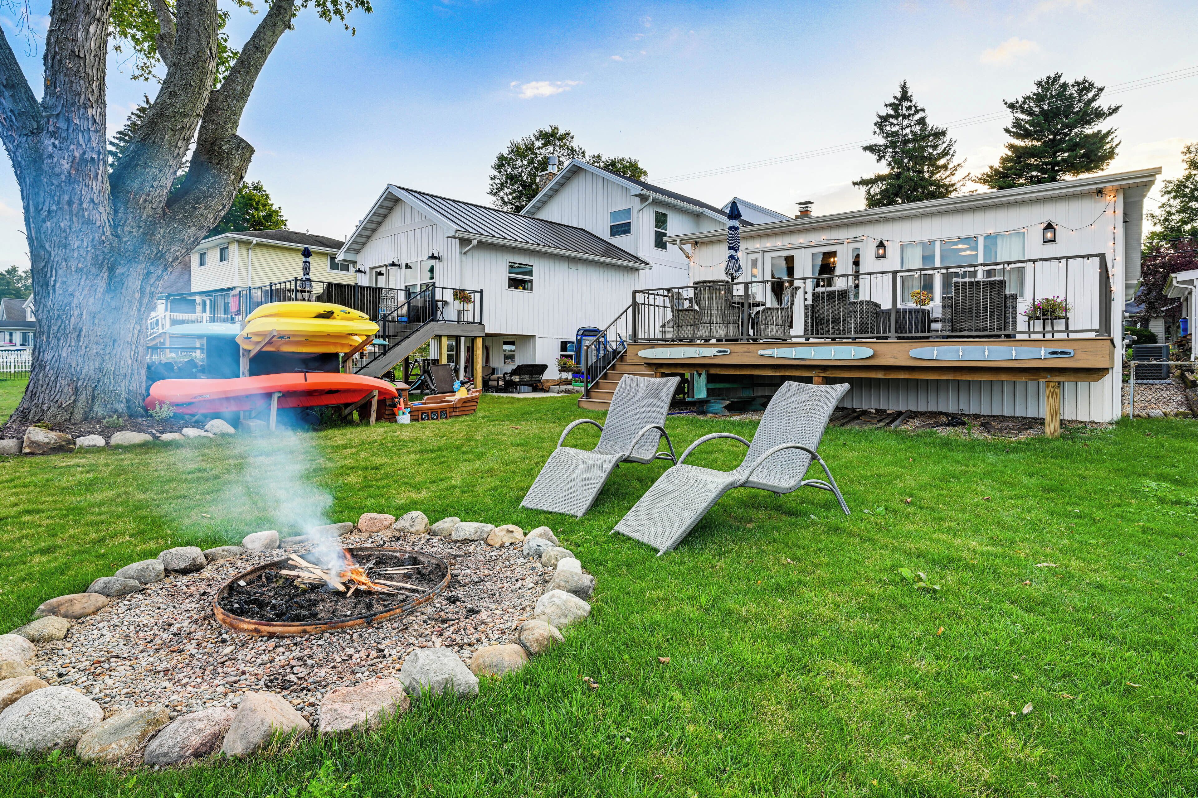 A backyard with a fire pit, lounge chairs, kayaks, and a deck with outdoor seating.