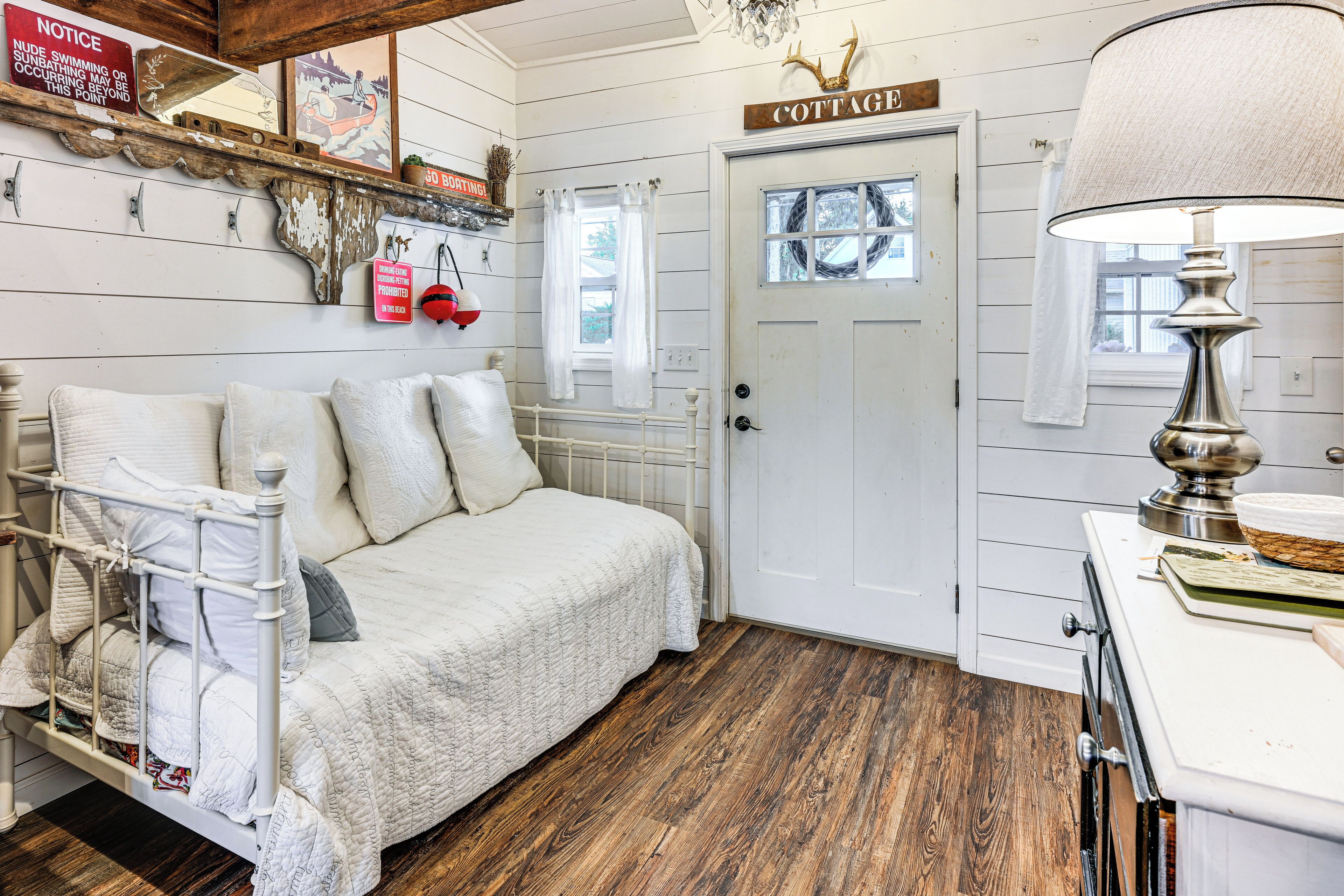 Een knus slaapkamer met een bed, een dressoir, een lamp en een deur met de tekst 'COTTAGE'.