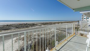 Vista da un balcone su una spiaggia, con una strada e vegetazione rada.