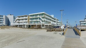Un hotel sulla spiaggia con numerosi balconi, una passerella in legno e un cielo azzurro limpido.