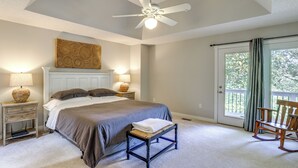 Ein Schlafzimmer mit einem Bett, Nachttischlampen, einem Deckenventilator, einer Bank, einem Schaukelstuhl und Blick ins Freie durch eine Schiebetür.