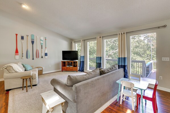 A living room with a sofa, a TV, a small table, and a window with curtains. - Garfield Vacation Rental w/ Beaver Lake Access! (Garfield)