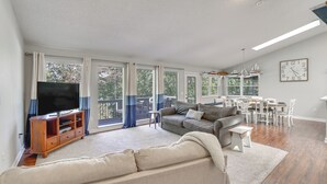 Ein geräumiges Wohnzimmer mit einer großen Couch, einem Fernseher und einem Essbereich mit Tisch und Stühlen.