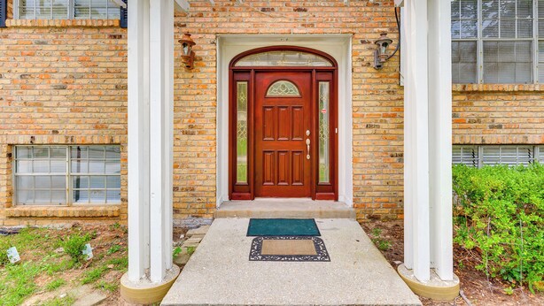 A brick building with a red door, white columns, and a green doormat. - Walkable Mobile Apartment w/ Fenced-in Yard (Mobile)