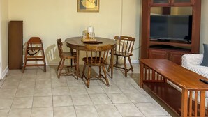 A dining area with a round table, four wooden chairs, a cabinet with a television, and a bench. - Walkable Mobile Apartment w/ Fenced-in Yard (Mobile)