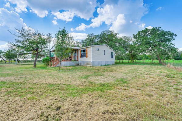 A single-story house with a porch, surrounded by a grassy field and trees. - Country Harwood Retreat: Trails, Creek & Wildlife (Harwood)