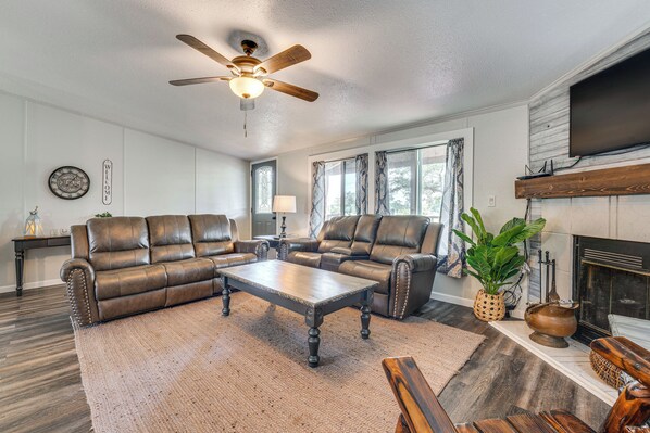 A living room with leather sofas, a wooden coffee table, a ceiling fan, and a fireplace. - Country Harwood Retreat: Trails, Creek & Wildlife (Harwood)