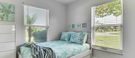 Ein Schlafzimmer mit einem Bett, einer Kommode und zwei Fenstern mit Jalousien.