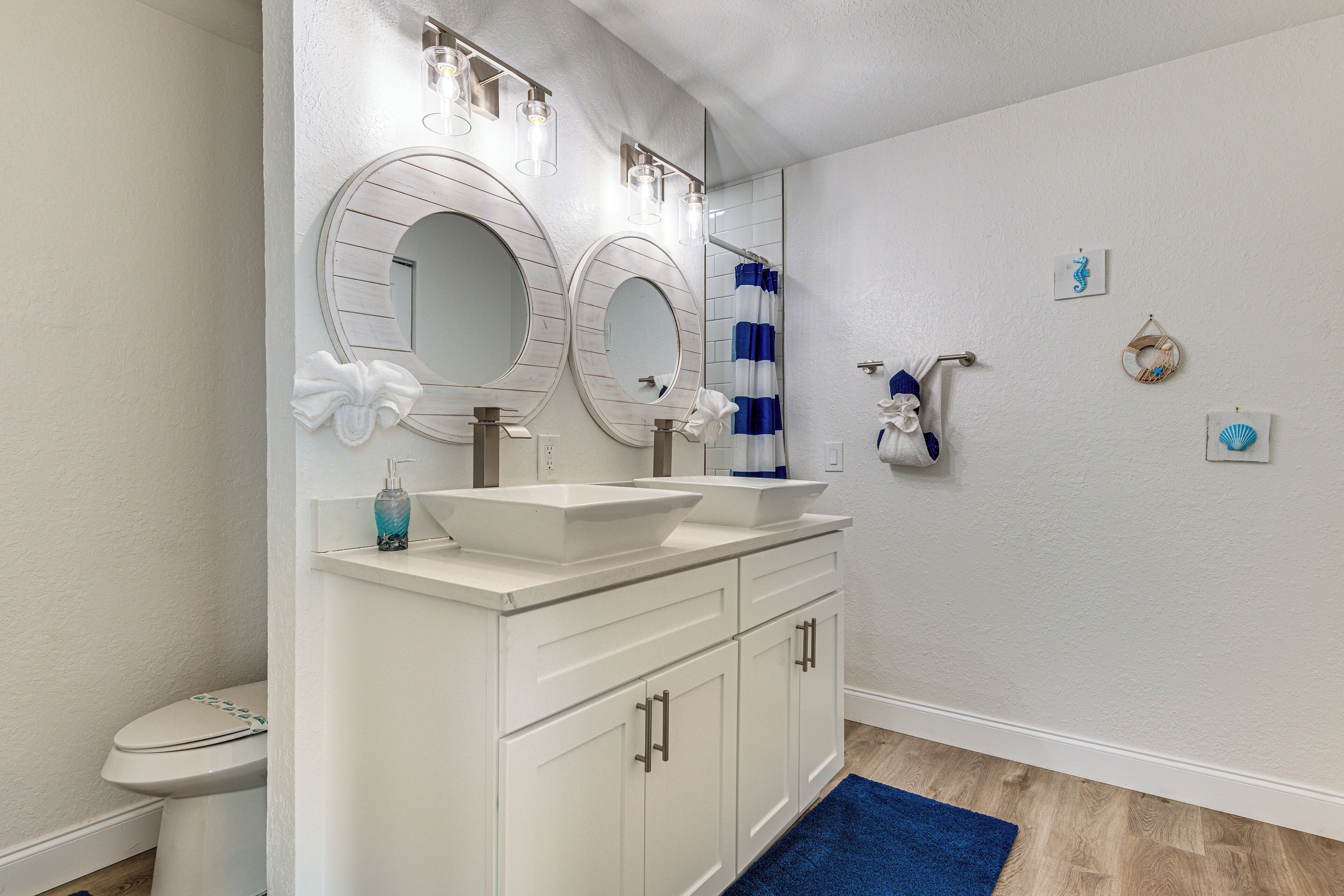 A bathroom with a white vanity, two sinks, a toilet, and a shower curtain.