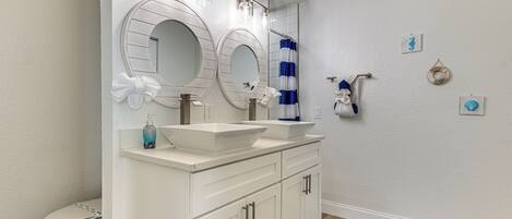 A bathroom with a white vanity, two sinks, a toilet, and a shower curtain.