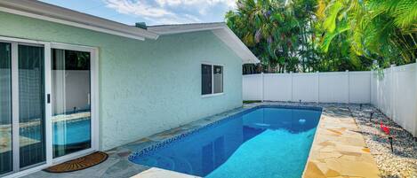 A swimming pool with stone tiles, a sliding glass door, and a white fence.