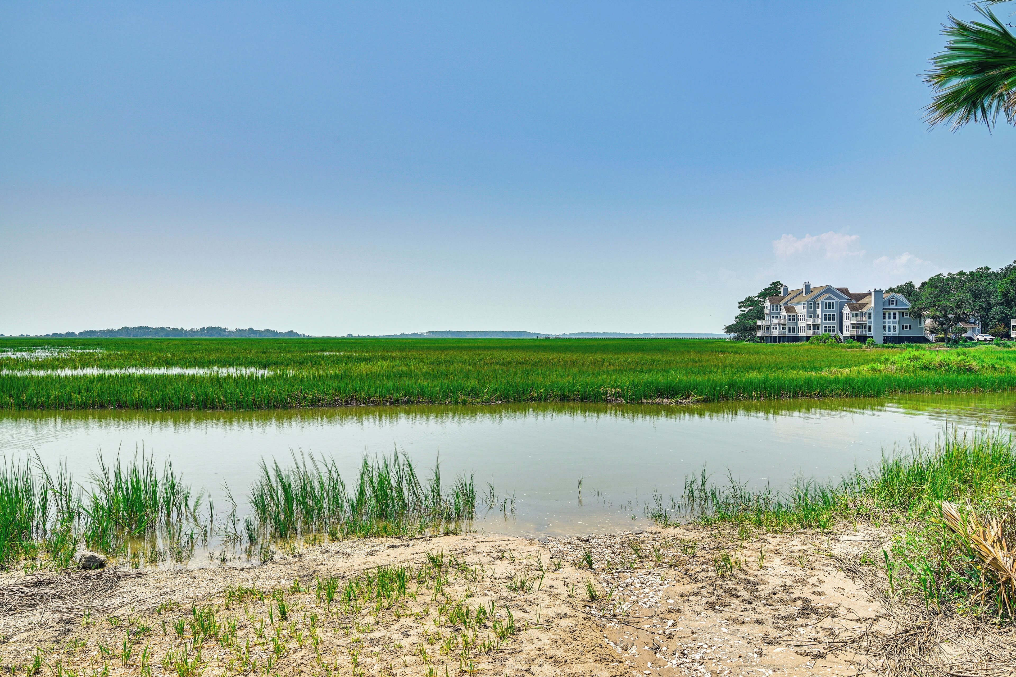 Une grande maison avec une vaste pelouse et un étang au premier plan.