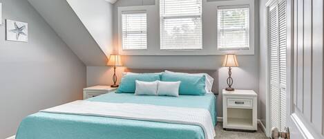 A bedroom with a sloped ceiling, a bed with teal bedding, two bedside lamps, and a nightstand with a drawer.