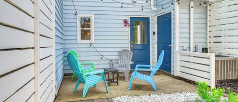 Une terrasse couverte, décorée de guirlandes lumineuses, avec deux chaises, une petite table et une porte.
