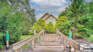 Un escalier en bois mène à une maison entourée d’une végétation luxuriante.
