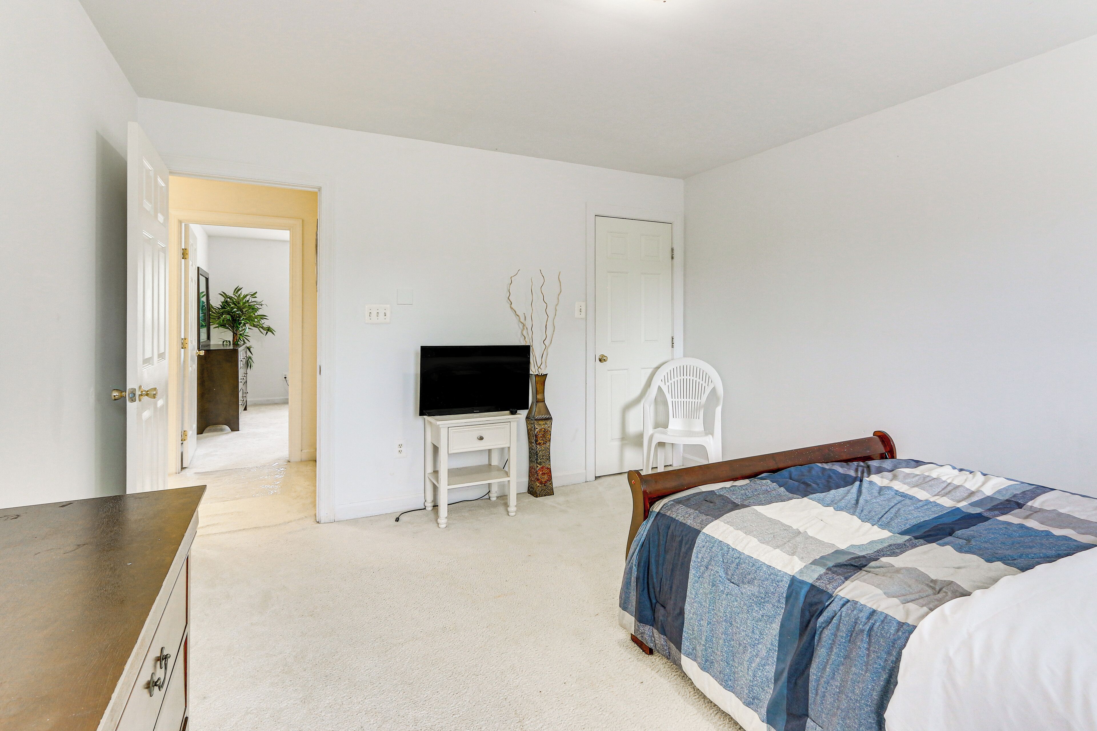 Un dormitorio con cama, cómoda, televisor sobre un mueble bajo y puerta que da a otra habitación.
