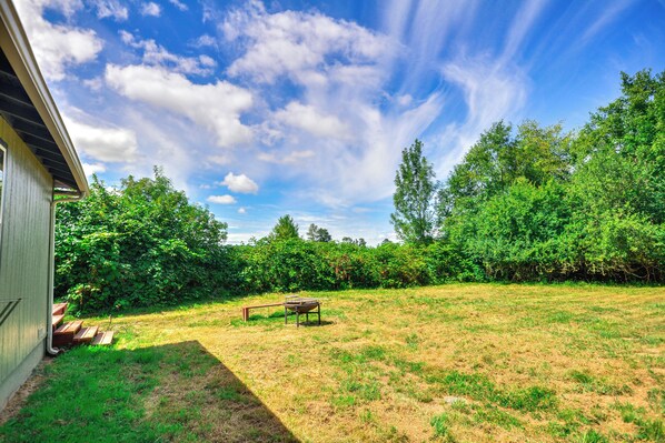 A grassy backyard with a wooden bench and a picnic table, surrounded by dense foliage and trees. - Private PNW Getaway on Puget Island! (Cathlamet)