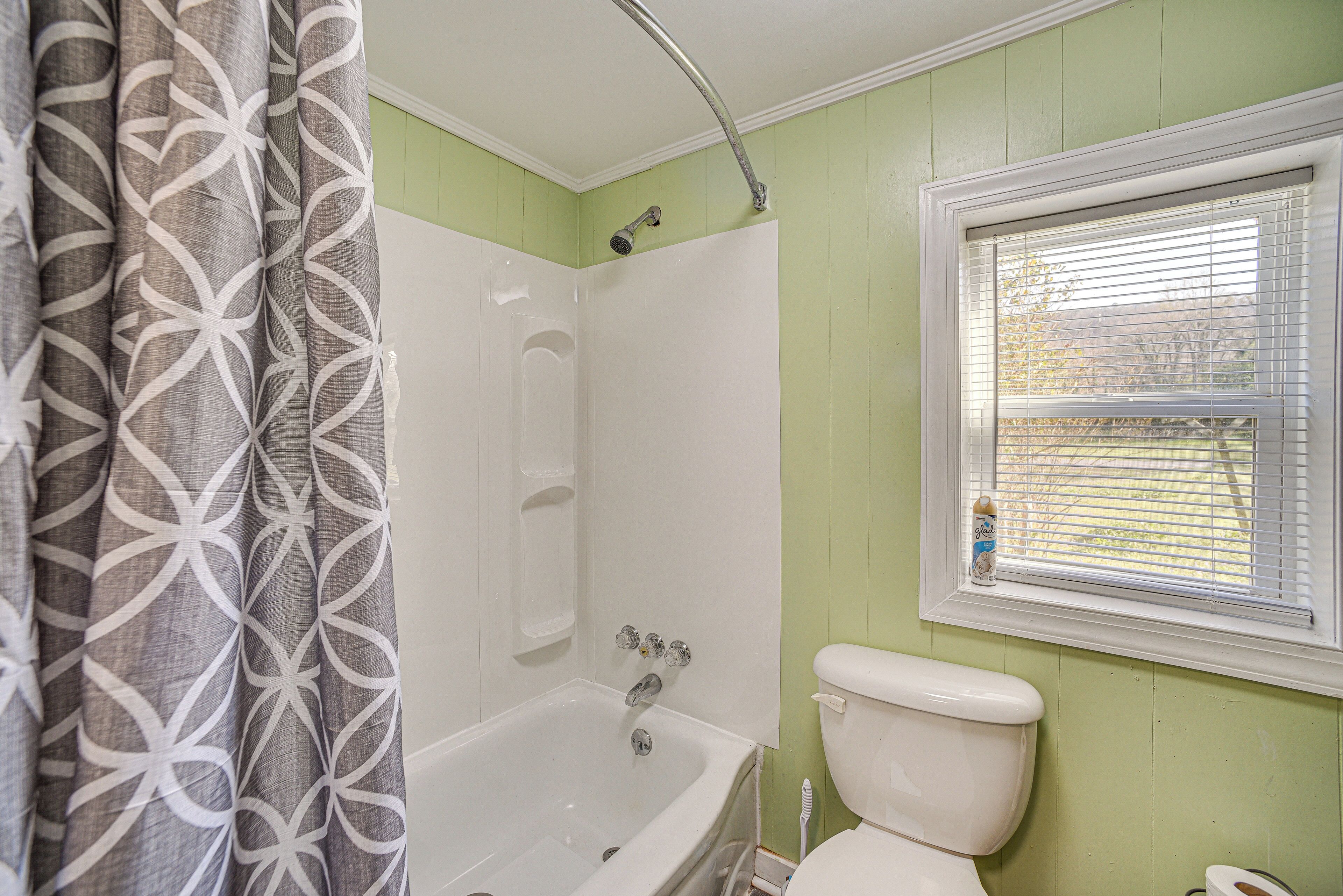 A bathroom with a bathtub, toilet, and window with blinds.