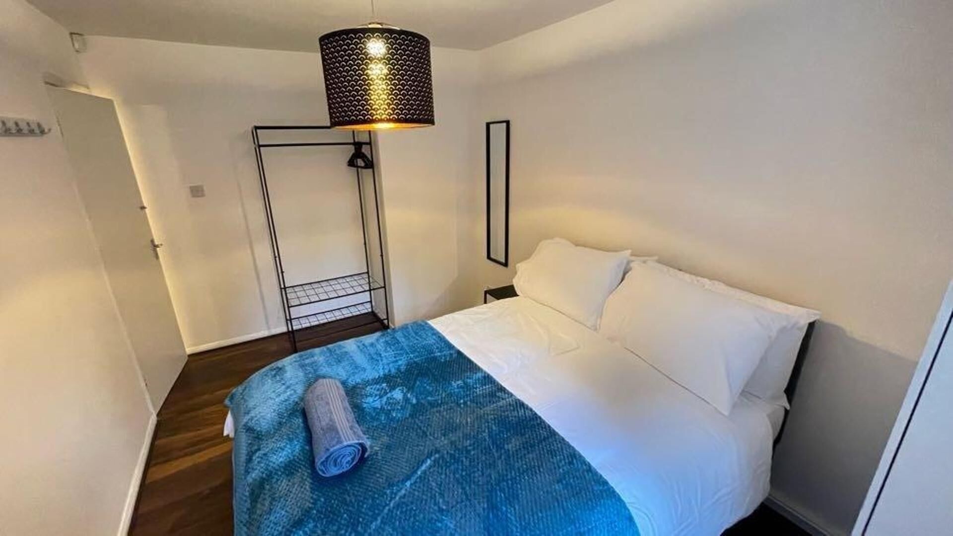 Un dormitorio con una cama, una colcha azul, una lámpara colgante negra y una puerta blanca.