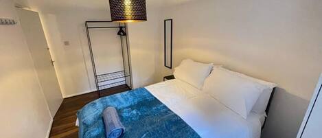 Un dormitorio con una cama, una colcha azul, una lámpara colgante negra y una puerta blanca.