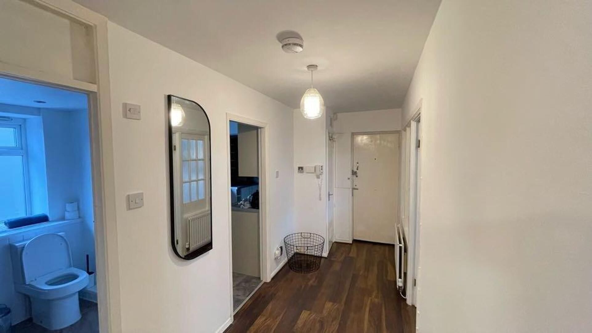 A hallway with a white door, a mirror, a radiator, and a hanging light fixture.