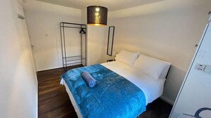 A hotel room with a bed, a blue blanket, a hanging light fixture, and a coat rack. - Melville Road Apartment - Birmingham City Centre (Birmingham)