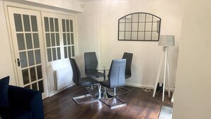 A dining area with a glass table and four chairs, a blue sofa, a lamp, and a radiator. - Melville Road Apartment - Birmingham City Centre (Birmingham)