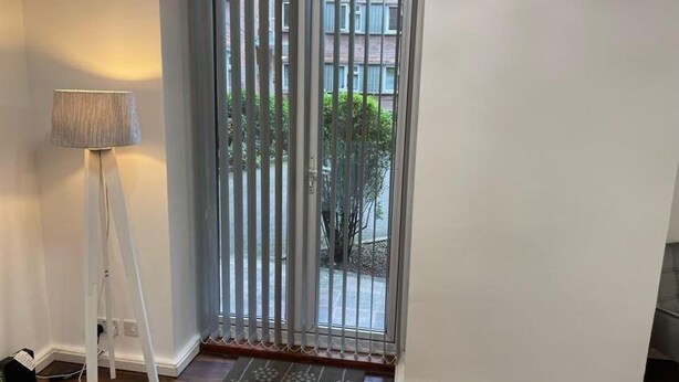 A room with a sliding glass door leading to a balcony, a floor lamp, and a doormat. - Melville Road Apartment - Birmingham City Centre (Birmingham)