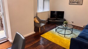A living room with a sofa, a coffee table, a TV, and a window with blinds. - Melville Road Apartment - Birmingham City Centre (Birmingham)