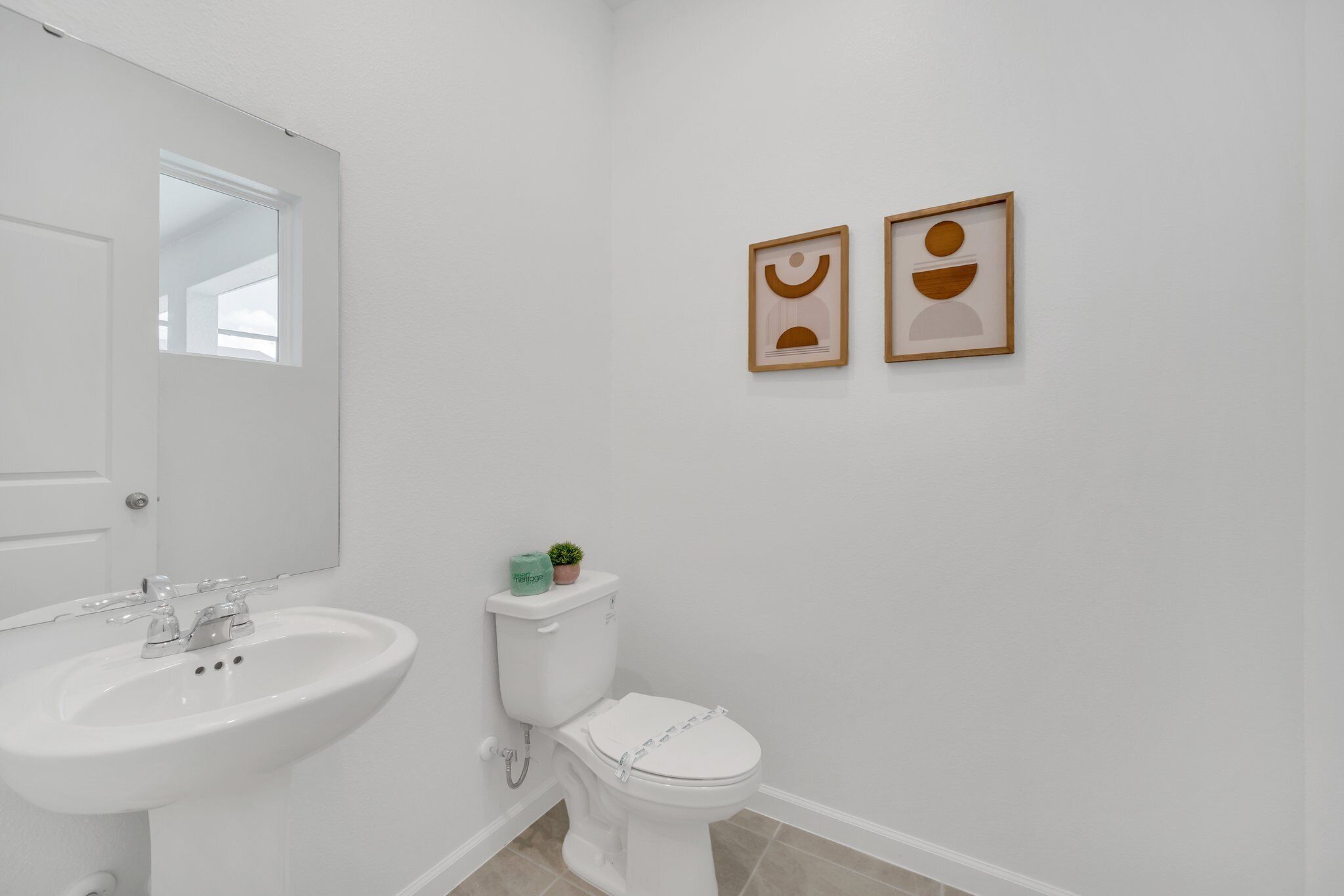 A bathroom with a white sink, toilet, and two framed pictures on the wall.