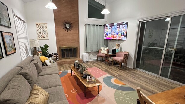 A living room with a sofa, a coffee table, and a TV. There is a fireplace and a window with curtains.