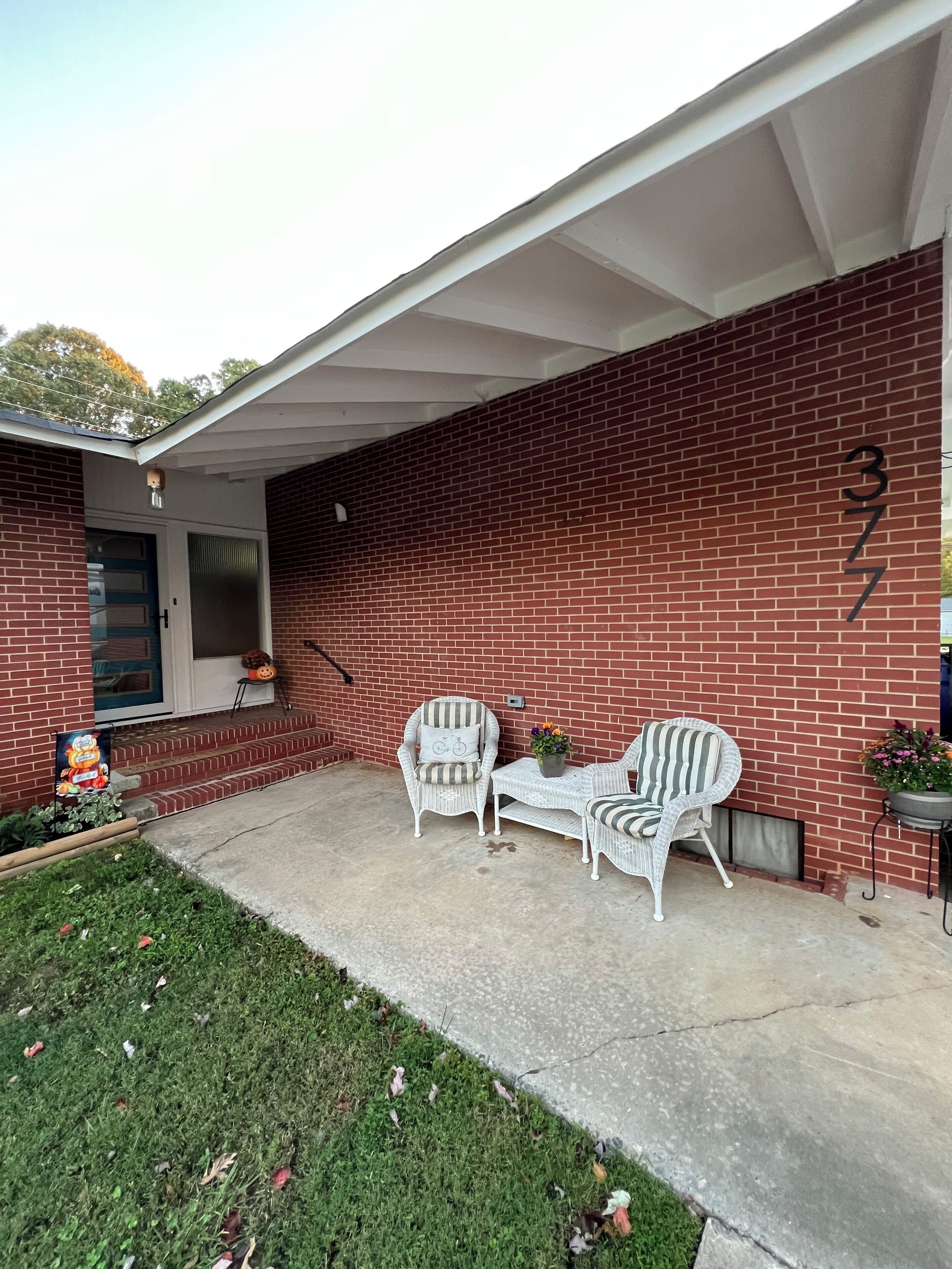 A brick house with a covered patio, two wicker chairs, a small table, and a potted plant.