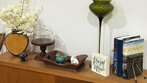 A wooden desk with a framed painting, a green vase, a bird figurine, a small sign, and books.
