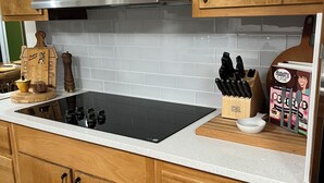 A kitchen with wooden cabinets, a stainless steel range hood, a black induction cooktop, and a white tiled backsplash.