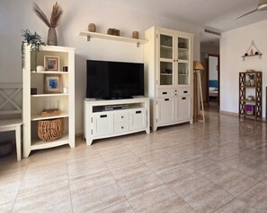 A living room with a flat-screen TV, white cabinets, a shelf with decorative items, and a wicker basket. - Delfines VII bl.II 2º Solo Familias! (Xeraco Playa)