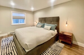 Un dormitorio con una cama grande, una ventana con persianas, una mesita de noche y un tapete estampado.