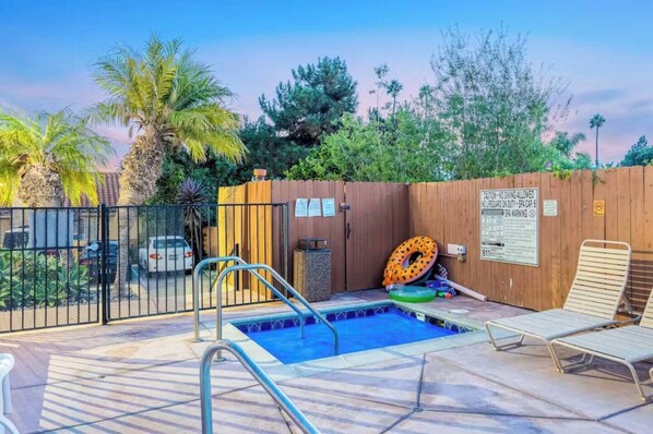 A backyard with a swimming pool, lounge chairs, and a wooden fence.
