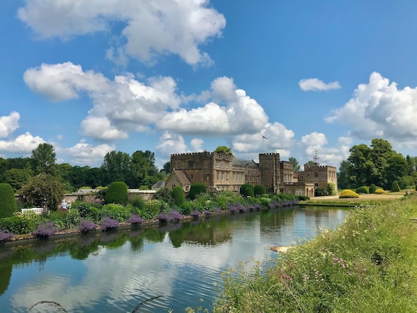 Un castillo histórico con un foso, rodeado de exuberante vegetación y un cielo despejado.