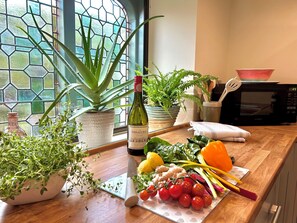 Una encimera de cocina con diversas plantas, una botella de vino, verduras frescas y utensilios de cocina.