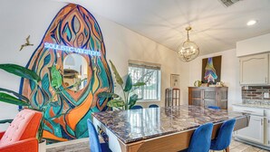 Un coin repas avec une grande table, des chaises bleues et un tableau abstrait aux couleurs vives accroché au mur.