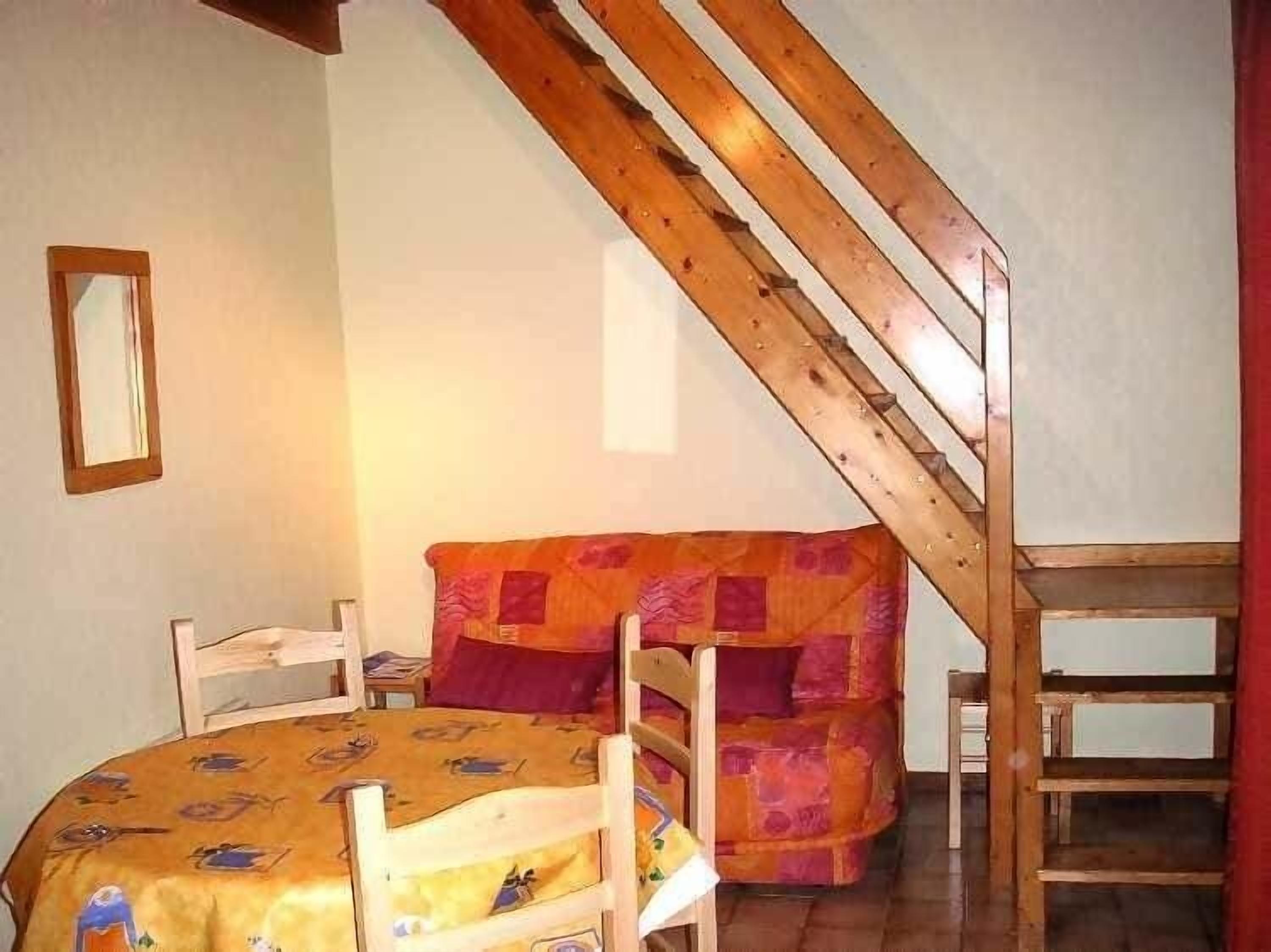 A bedroom with a wooden staircase, a bed with a patterned bedspread, and a chair.