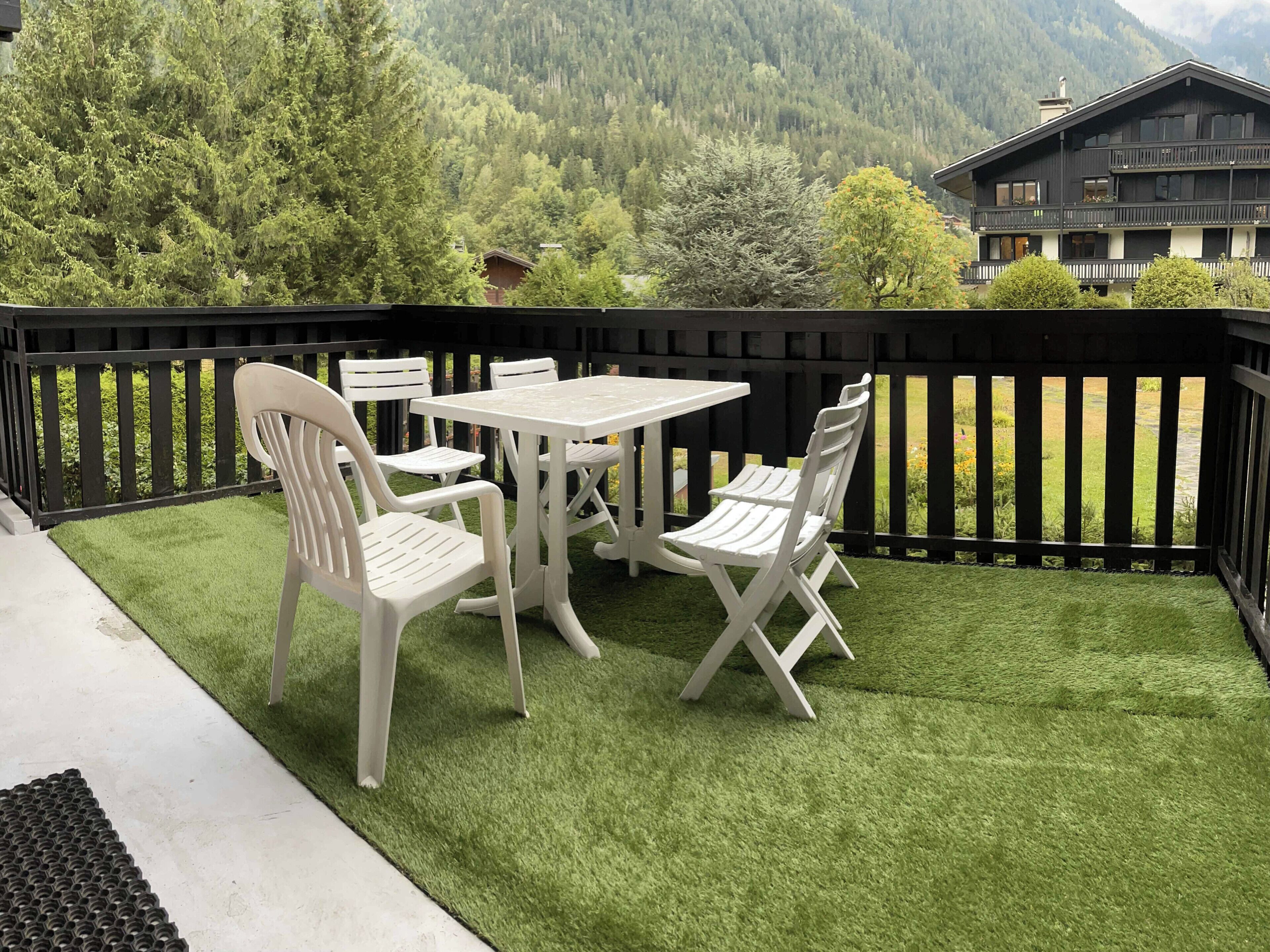 A balcony with a table and chairs, surrounded by a black railing, overlooking a mountainous landscape.