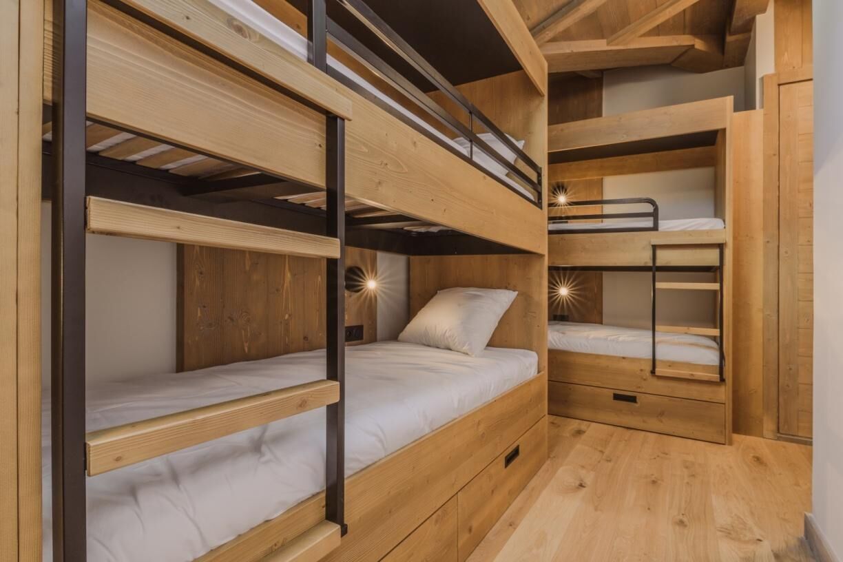 Een slaapkamer met stapelbed, houten wanden en vloeren, een klein bureau en nachtkastje.