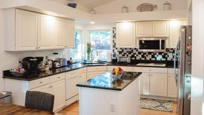 A modern kitchen with white cabinets, a black countertop, a central island, a microwave, a refrigerator, and a window providing natural light.