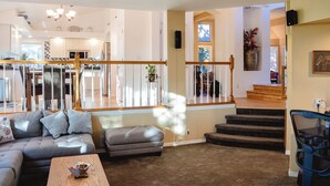 A spacious living area with a sofa, ottoman, and coffee table. A staircase leads to a second floor with a kitchen and dining area.