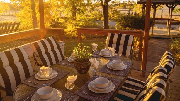An outdoor dining area with striped cushioned seating, a table set for a meal, and a gazebo in the background.