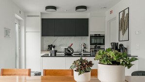 A modern kitchen with dark cabinets, a marble backsplash, and a dining area with a wooden table and chairs. There are two potted plants on the table. - Huize Marie-Beau with spacious garden (Peer)