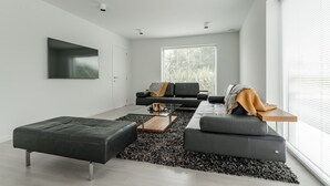 A modern living room with a black leather sofa, a glass coffee table, and a black shag rug. - Huize Marie-Beau with spacious garden (Peer)
