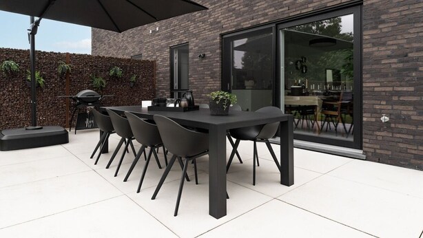 A modern outdoor patio with a black table and chairs, a large umbrella, and a brick wall with plants. - Huize Marie-Beau with spacious garden (Peer)