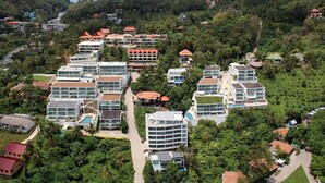 A resort with multiple buildings, including a large hotel with a swimming pool and a smaller building with a red roof. - Kata Ocean View 2BR Apartment O910 (Karon)
